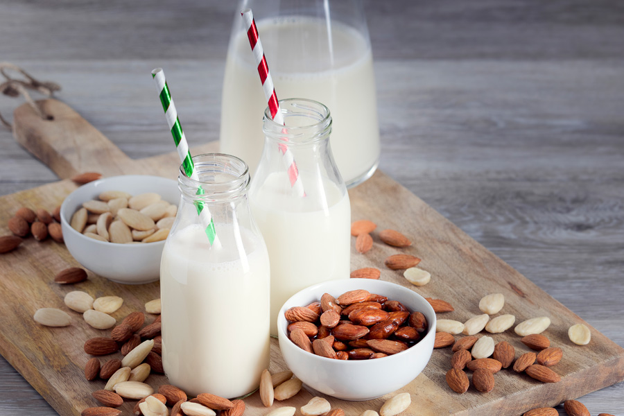 Recept på alkoholfri mandelcocktail Stämningsbild "alkoholfri mandelcocktail": två fyllda bredhalsade flaskor med färgglada sugrör står på en träskiva med mandel